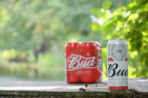 Budweiser Bud beer cans on old wooden table outdoors at the river and green trees background photo