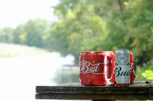 Budweiser Bud beer cans on old wooden table outdoors at the river and green trees background photo
