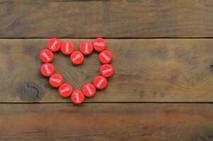 Heart of many red caps with coca cola logo on wooden background photo
