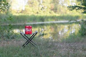 Budweiser Bud beer cans pack on folding chair outdoors at the river and green trees background photo