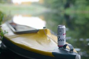 Budweiser Bud beer can on yellow kayak outdoors in the river and green trees blurred background photo