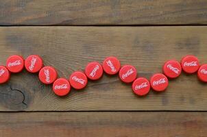 Many red caps with coca cola logo on wooden background photo