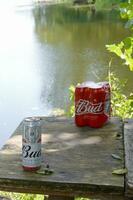 Budweiser Bud beer cans on old wooden table outdoors at the river and green trees background photo