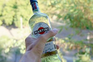 Bottle of Vermouth Martini Rossi in male hand on a green trees background photo