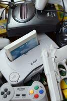 Pile of old 8-bit video game consoles and many gaming accessories like a joysticks and cartridges photo