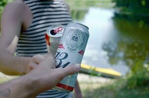 Young man raise Budweiser Bud beer can with male friend on blurred river with kayak and trees photo