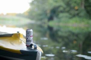 Budweiser Bud beer can on yellow kayak outdoors in the river and green trees blurred background photo