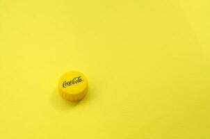 Single yellow bottle lid with Coca Cola logo on yellow background photo