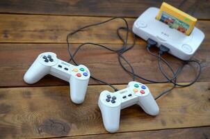 Old 8-bit video game console with game cartridge and two gaming joysticks on wooden background photo