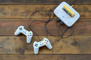 Old 8-bit video game console with game cartridge and two gaming joysticks on wooden background photo