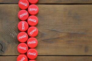 Many red caps with coca cola logo on wooden background photo