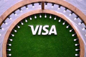 VISA logo on green grass in photozone with many white lightlamp bulbs ad wooden plank photo