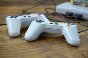 Old 8-bit video game console with game cartridge and two gaming joysticks on wooden background photo