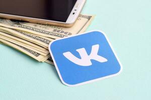 Vkontakte paper logo lies with envelope full of dollar bills and smartphone photo