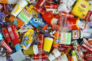 Big pile of many disposable colored trash from edible products of famous food and beverage manufacturers. Soda cans and chocolate bar wrappings in stack photo