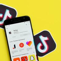 Tiktok application in playmarket on samsung smartphone screen on yellow background. TikTok is a popular video-sharing social networking service owned by ByteDance photo