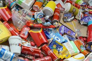 Big pile of many disposable colored trash from edible products of famous food and beverage manufacturers. Soda cans and chocolate bar wrappings in stack photo