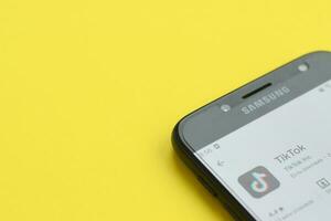 Tiktok application in playmarket on samsung smartphone screen on yellow background. TikTok is a popular video-sharing social networking service owned by ByteDance photo
