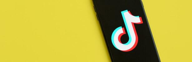 Tiktok logo on samsung smartphone screen on yellow background. TikTok is a popular video-sharing social networking service owned by ByteDance photo