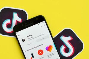 Tiktok application in playmarket on samsung smartphone screen on yellow background. TikTok is a popular video-sharing social networking service owned by ByteDance photo