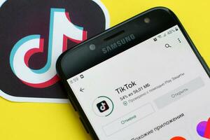 Tiktok application in playmarket on samsung smartphone screen on yellow background. TikTok is a popular video-sharing social networking service owned by ByteDance photo