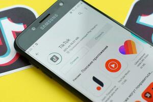 Tiktok application in playmarket on samsung smartphone screen on yellow background. TikTok is a popular video-sharing social networking service owned by ByteDance photo