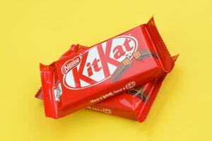 Kit Kat chocolate bar in red wrapping lies on yellow background. Kit kat created by Rowntree's of York in United Kingdom and is now produced globally by Nestle photo