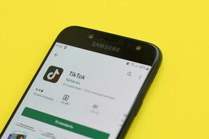 Tiktok application in playmarket on samsung smartphone screen on yellow background. TikTok is a popular video-sharing social networking service owned by ByteDance photo