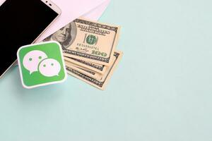 Wechat paper logo lies with envelope full of dollar bills and smartphone photo