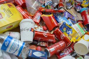 Big pile of many disposable colored trash from edible products of famous food and beverage manufacturers. Soda cans and chocolate bar wrappings in stack photo