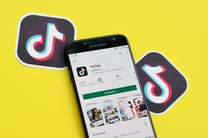 Tiktok application in playmarket on samsung smartphone screen on yellow background. TikTok is a popular video-sharing social networking service owned by ByteDance photo