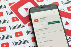 Youtube app on samsung smartphone screen on paper banner with small youtube logos and inscriptions. YouTube is Google subsidiary and American most popular video-sharing platform photo