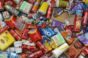 Big pile of many disposable colored trash from edible products of famous food and beverage manufacturers. Soda cans and chocolate bar wrappings in stack photo