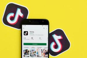 Tiktok application in playmarket on samsung smartphone screen on yellow background. TikTok is a popular video-sharing social networking service owned by ByteDance photo