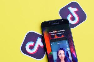 Tiktok application on samsung smartphone screen on yellow background. TikTok is a popular video-sharing social networking service owned by ByteDance photo