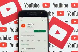 Youtube app on samsung smartphone screen on paper banner with small youtube logos and inscriptions. YouTube is Google subsidiary and American most popular video-sharing platform photo