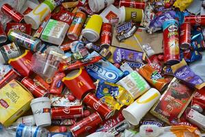 Big pile of many disposable colored trash from edible products of famous food and beverage manufacturers. Soda cans and chocolate bar wrappings in stack photo