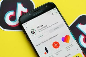 Tiktok application in playmarket on samsung smartphone screen on yellow background. TikTok is a popular video-sharing social networking service owned by ByteDance photo