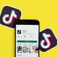 Tiktok application in playmarket on samsung smartphone screen on yellow background. TikTok is a popular video-sharing social networking service owned by ByteDance photo