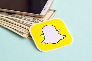 Snapchat paper logo lies with envelope full of dollar bills and smartphone photo