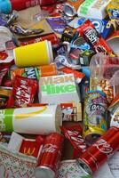 Big pile of many disposable colored trash from edible products of famous food and beverage manufacturers. Soda cans and chocolate bar wrappings in stack photo