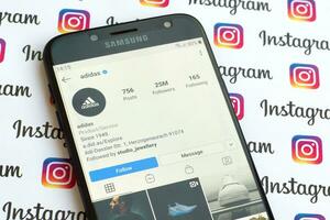 Adidas official instagram account on smartphone screen on paper instagram banner. photo