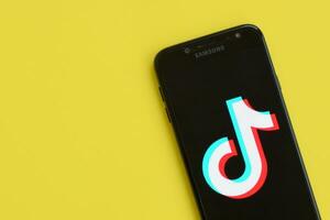 Tiktok logo on samsung smartphone screen on yellow background. TikTok is a popular video-sharing social networking service owned by ByteDance photo