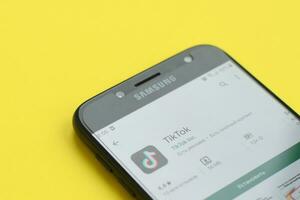Tiktok application in playmarket on samsung smartphone screen on yellow background. TikTok is a popular video-sharing social networking service owned by ByteDance photo