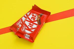 Kit Kat chocolate bars in red wrapping lies on yellow and red background. Kit kat created by Rowntree's of York in United Kingdom and is now produced globally by Nestle photo