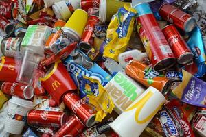 Big pile of many disposable colored trash from edible products of famous food and beverage manufacturers. Soda cans and chocolate bar wrappings in stack photo