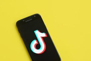 Tik Tok logo en Samsung teléfono inteligente pantalla en amarillo antecedentes. Tik Tok es un popular compartir videos social redes Servicio poseído por bytedance foto