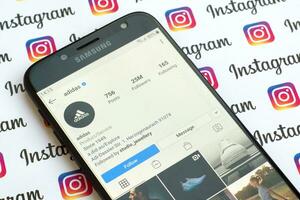 Adidas official instagram account on smartphone screen on paper instagram banner. photo