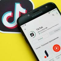 Tiktok application in playmarket on samsung smartphone screen on yellow background. TikTok is a popular video-sharing social networking service owned by ByteDance photo