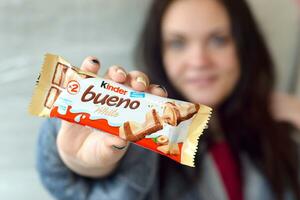 joven mujer muestra más amable bueno blanco chocolate caramelo bar en de colores envase. más amable bueno por italiano confitería fabricante ferrero foto